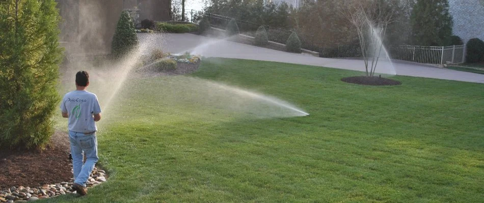 Sprinklers running on a lawn in Enochville, NC, with a worker.