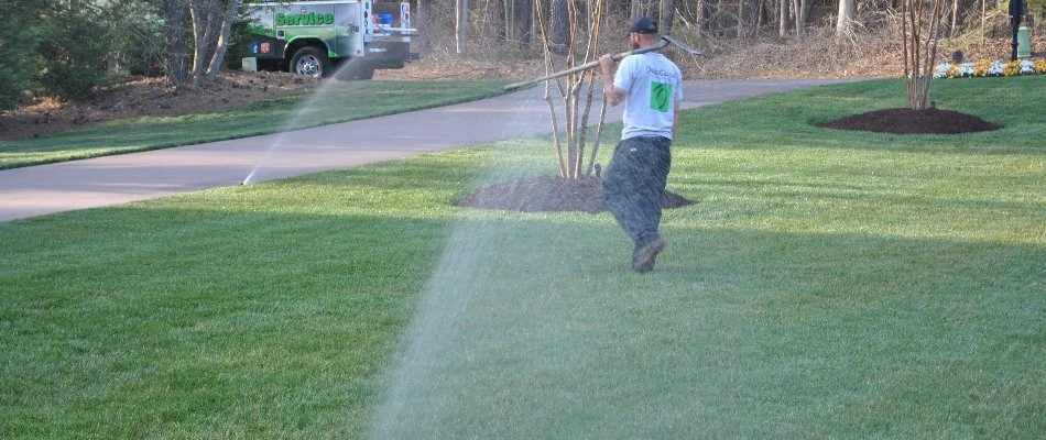 Tech walking across a lawn with running sprinklers in Allen, NC.